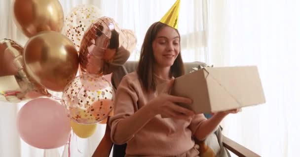 Jonge vrouw in verjaardagshoed schudt grote papieren doos met geschenk — Stockvideo