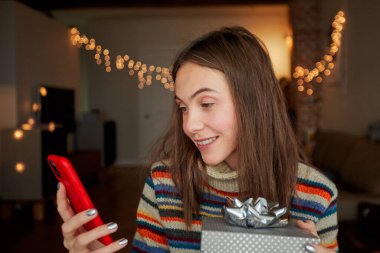 Noel hediyeli neşeli kadın akıllı telefon kullanıyor.
