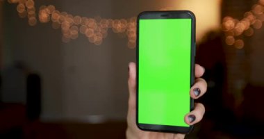 Gümüş manikürlü genç kadın eli yeşil akıllı telefonu tutuyor.