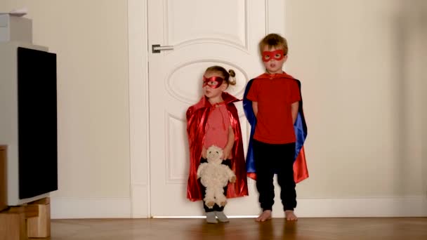 Kırmızı süper kahraman kostümlü komik çocuklar ellerinde oyuncaklarla dolaşıyorlar. — Stok video