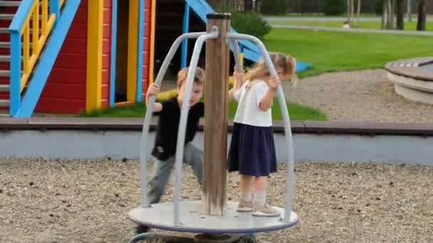 Boy and girl ride merry-go-round spending time on playground — Stock Video