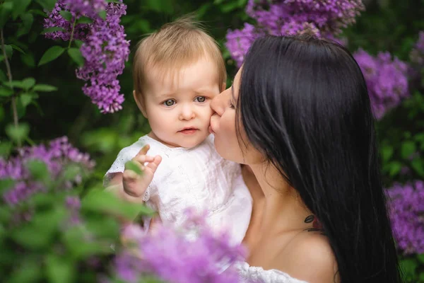 A mãe beija a filha perto de um lilás florescente. Cor roxa. Imagem de primavera — Fotografia de Stock