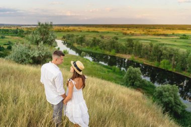 genç çift el ele çayır boyunca yürüyor. Birbiriniz bakıyor.