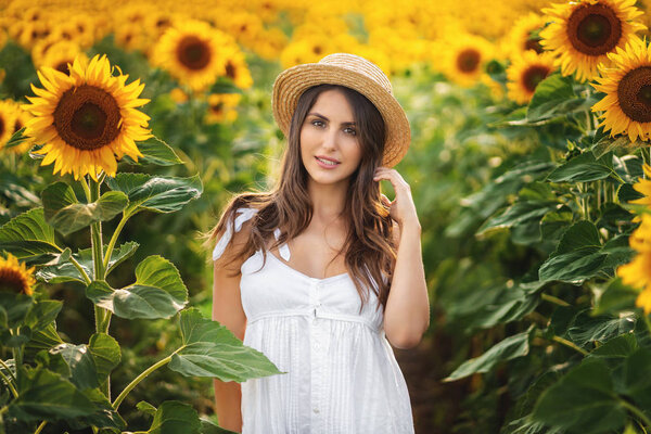 Outdoor portrait of young beautiful happy smiling girl wearing straw hat . posing at sunflower field