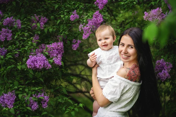 Giovane madre con adorabile bambino in una passeggiata nel parco fiorito. Albero lilla su uno sfondo. Ritratto sorridente — Foto Stock