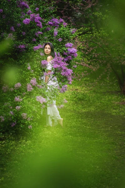 Piękna młoda kobieta w długiej białej sukni z kwitnącymi drzewami w wiosennym ogrodzie. — Zdjęcie stockowe