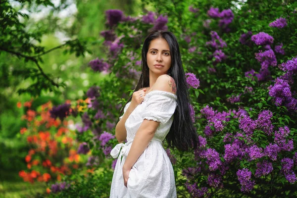 Młoda kobieta z długimi włosami, ubrana w białą sukienkę stwarzające w kwitnącym ogrodzie — Zdjęcie stockowe