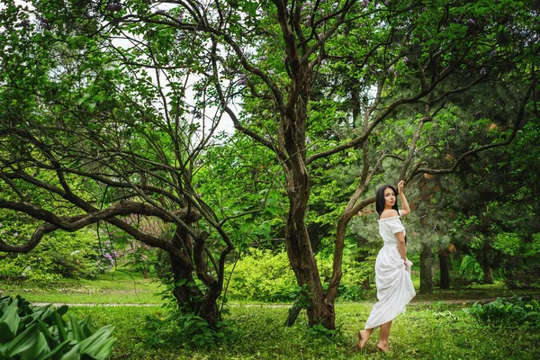 Hermosa joven vestida con elegante vestido blanco caminando por un sendero forestal — Foto de Stock