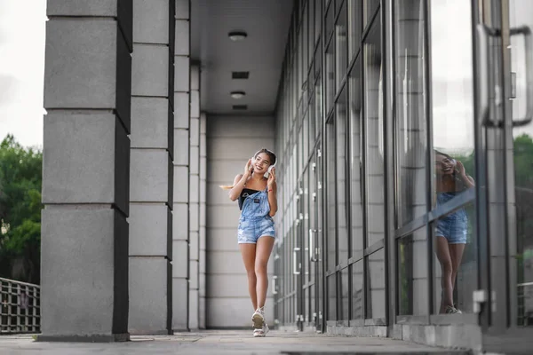 휴대 전화와 이어폰으로 걷는 매력적인 젊은 십대 소녀의 사진 — 스톡 사진