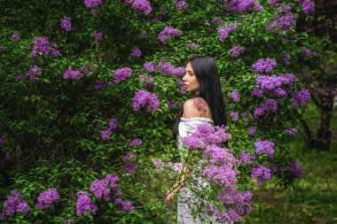 çıplak omuzları ile büyük bir elbise giymiş bir dövme kız parkta çiçekler koklar