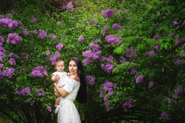 Mãe com tatuagem e seu bebê entre flores de jardim ao ar livre . — Fotografia de Stock