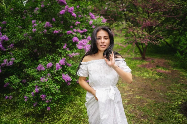 Młoda kobieta z długimi ciemnymi włosami pozowanie w pobliżu drzewa z fioletowymi kwiatami. Jej fala włosa od wiatru. Fotografia w ruchu — Zdjęcie stockowe