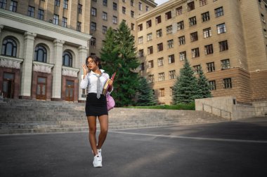 Gözlük, beyaz bir gömlek ve siyah bir etek güzel bir genç Afrikalı Amerikalı kız elinde ders kitapları tutuyor