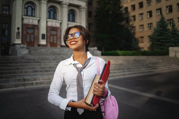 大学の背景でバックパックを持つ幸せな笑顔アフリカ系アメリカ人の学生の女の子. — ストック写真