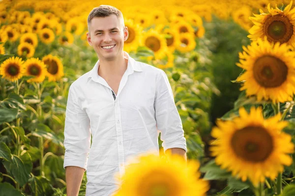 Joven hombre feliz sonriendo a la cámara en el campo de girasoles —  Fotos de Stock