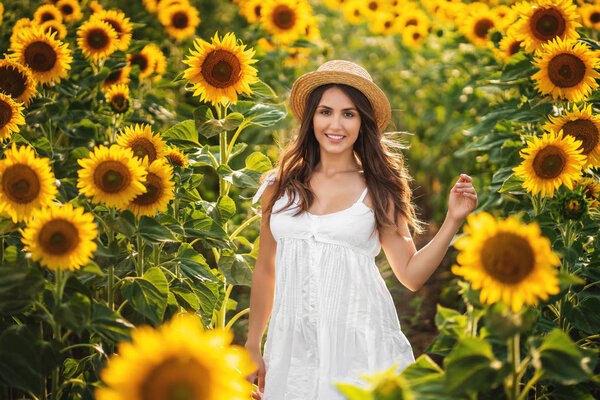 sweet girl in a white dress walking on a field of sunflowers