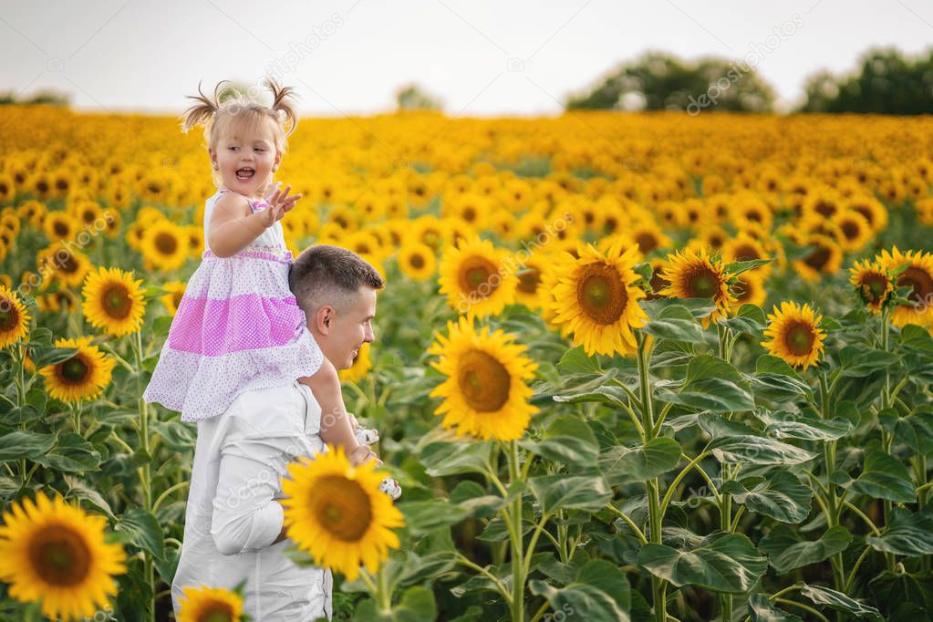Dad walks with his daughter on a field with a sunflower. 