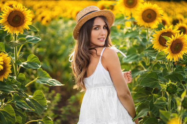 A beautiful young woman in a summer dress and straw hat walks al