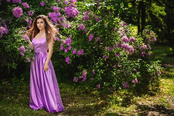 Muchacha atractiva cerca de un árbol de color lila en flor. Su pelo revolotea en el viento —  Fotos de Stock