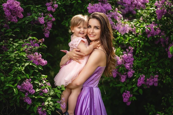 Una donna sorridente con un bambino in passeggiata. Alberi lilla in fiore su — Foto Stock