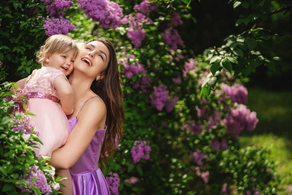 Mulher rindo com menina em uma caminhada. Floração lilás árvores em — Fotografia de Stock