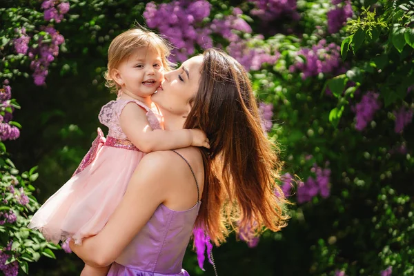 Mãe está segurando sua filha feliz e beijando sua bochecha — Fotografia de Stock