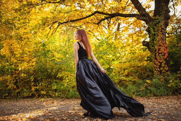 Redhead woman in long dress walking at autumn park