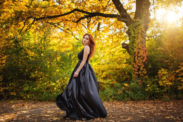 Tender girl in a black dress strolls against the background of fiery autumn nature.