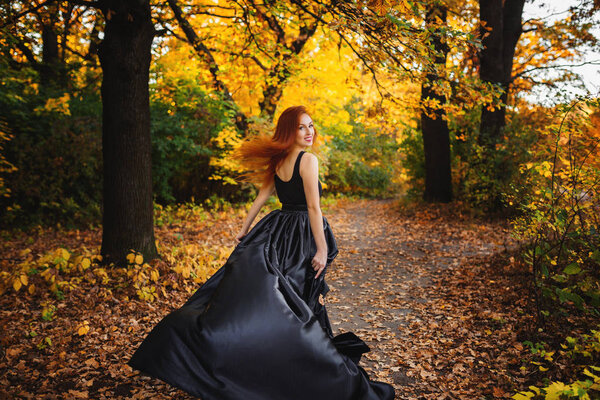 Authentic girl on a walk in autumn park. Long red hair develops in the wind.