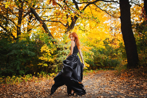 Young beautiful redhead woman in long black dress in autumn forest. female. freedom