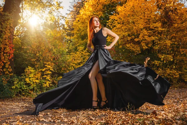 Mooie jonge vrouw met zeer lang rood haar in een zwarte jurk w Stockfoto