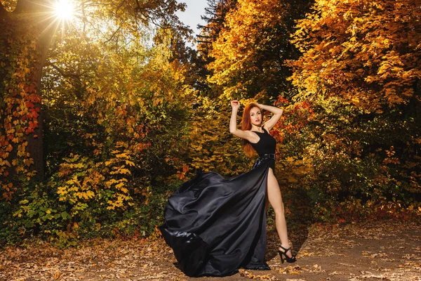Roodharige vrouw in lange blac jurk op fantastische herfst bos Stockafbeelding
