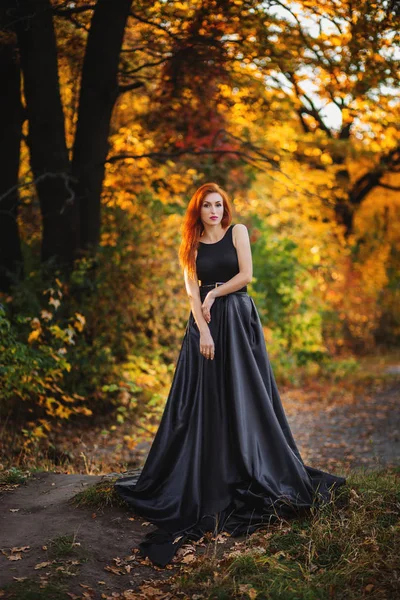 Stijlvolle roodharige meisje op mooie herfst alley. Stockfoto