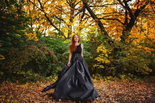 Fantastiske rødhårede model i sort kjole ser på kamera og po Royaltyfrie stock-fotos