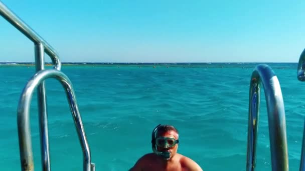 Um homem com uma máscara de mergulho está subindo uma escada para fora da água — Vídeo de Stock