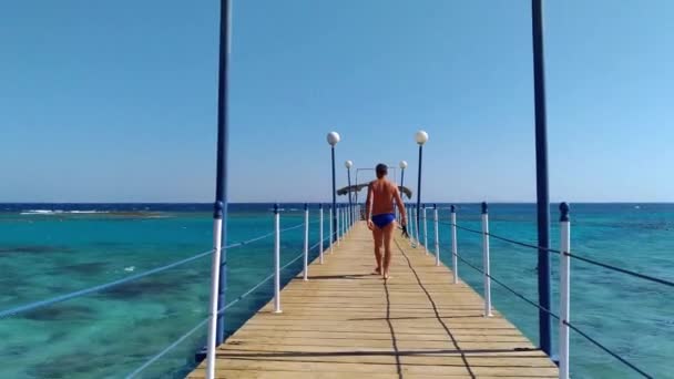 El hombre camina tranquilamente a lo largo del muelle hacia el mar — Vídeos de Stock