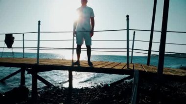 Adam tebrik elinde yükseltir. Bir adam bir iskele deniz kenarında duruyor