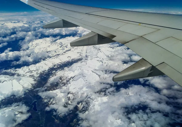 Mountains and white snow on the tops under the wing of the aircraft during the flight