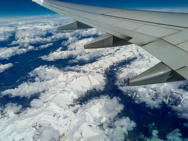 Βουνά και λευκό χιόνι στις κορυφές κάτω από την πτέρυγα του αεροσκάφους κατά τη διάρκεια της πτήσης — Φωτογραφία Αρχείου