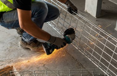 Sanayi işçisi, öğütücüyle metal kesiyor. Görünür kıvılcımlar. 