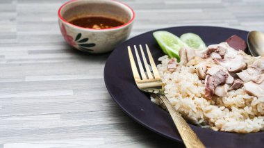 chicken rice with rich broth-infused grains, cucumber slices, and congealed bloodserved with golden utensils on a rustic wooden table.