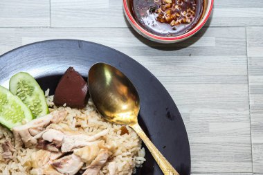 chicken rice with rich broth-infused grains, cucumber slices, and congealed bloodserved with golden utensils on a rustic wooden table.