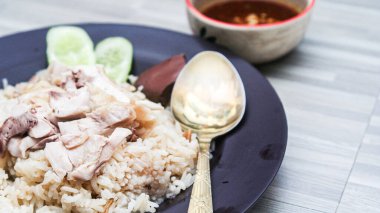chicken rice with rich broth-infused grains, cucumber slices, and congealed bloodserved with golden utensils on a rustic wooden table.