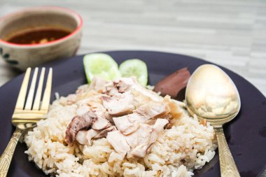 chicken rice with rich broth-infused grains, cucumber slices, and congealed bloodserved with golden utensils on a rustic wooden table.