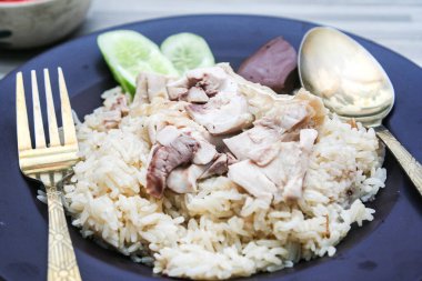 chicken rice with rich broth-infused grains, cucumber slices, and congealed bloodserved with golden utensils on a rustic wooden table.