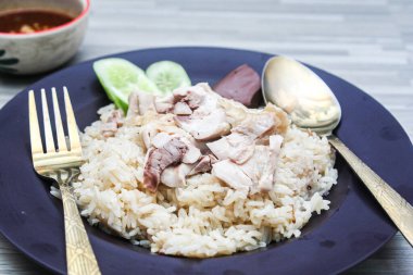 chicken rice with rich broth-infused grains, cucumber slices, and congealed bloodserved with golden utensils on a rustic wooden table.