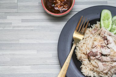 chicken rice with rich broth-infused grains, cucumber slices, and congealed bloodserved with golden utensils on a rustic wooden table.