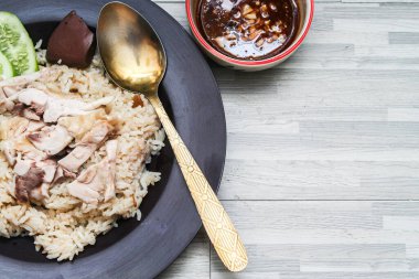 chicken rice with rich broth-infused grains, cucumber slices, and congealed bloodserved with golden utensils on a rustic wooden table.