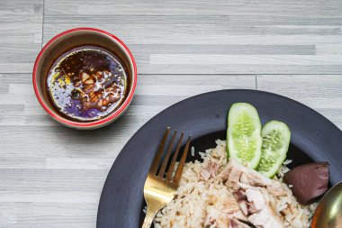 chicken rice with rich broth-infused grains, cucumber slices, and congealed bloodserved with golden utensils on a rustic wooden table.