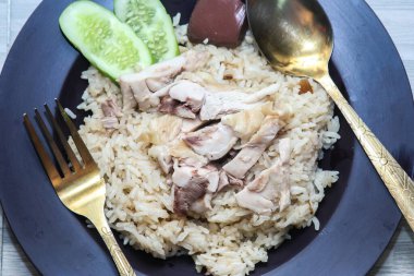 chicken rice with rich broth-infused grains, cucumber slices, and congealed bloodserved with golden utensils on a rustic wooden table.